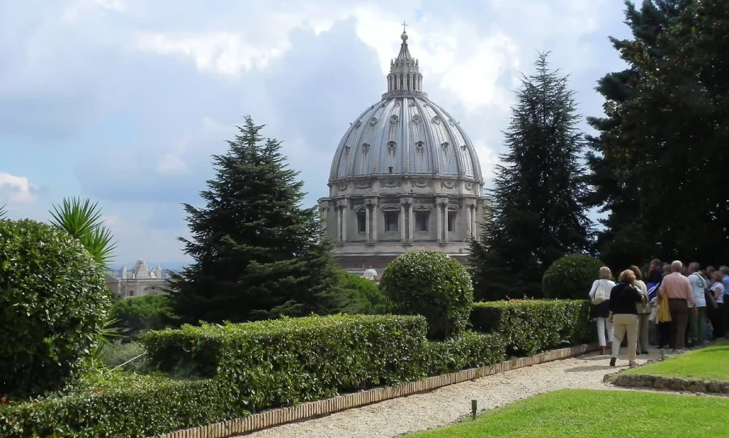 A group walks through the Vatican Gardens with St. Peter’s Dome in the background